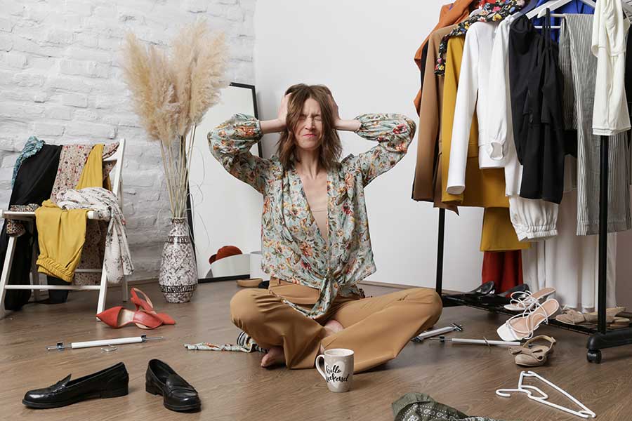 A photograph of a woman in her Living space with her head in her hands surrounded by clutter