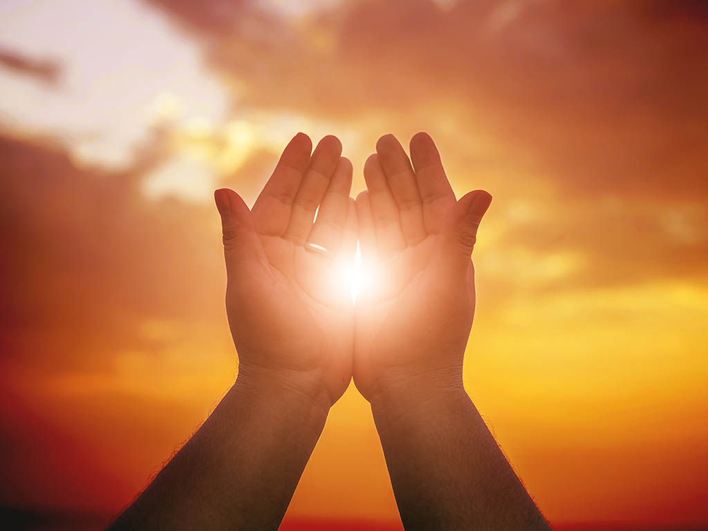 Reiki healing: two hands held together with the sun shining between them, representing reiki energy